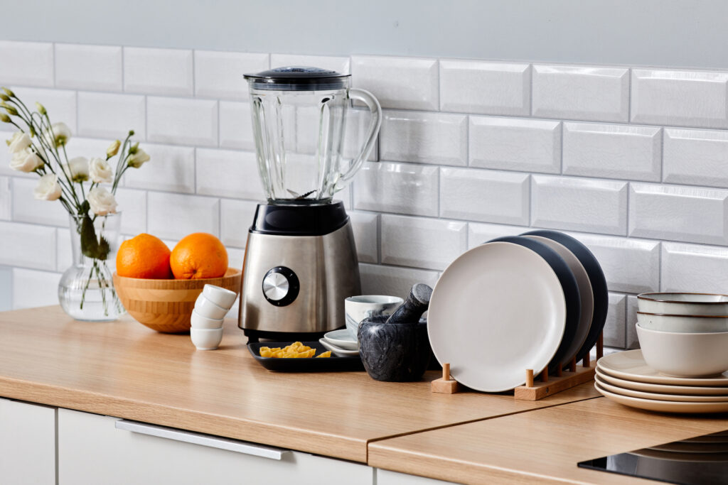 Image of electric blender, set of ceramic plates and other kitchen wares on table in kitchen