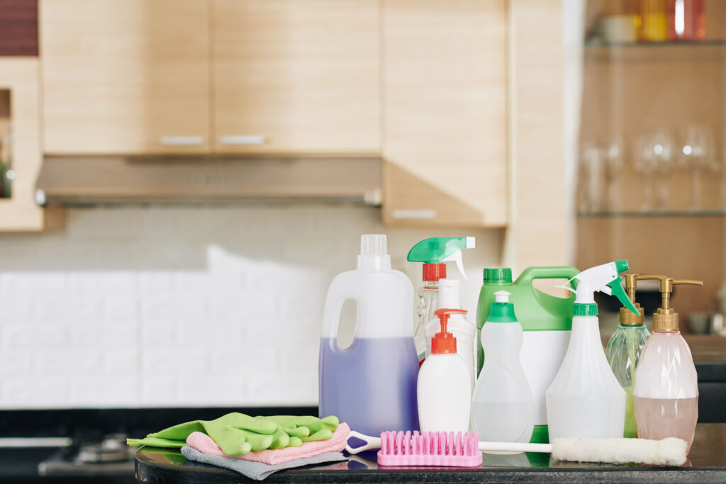 Set for house cleaning: plastic bottles with detergents and disinfecting sprays on kitchen counter with rubber gloves, broshes and cloth