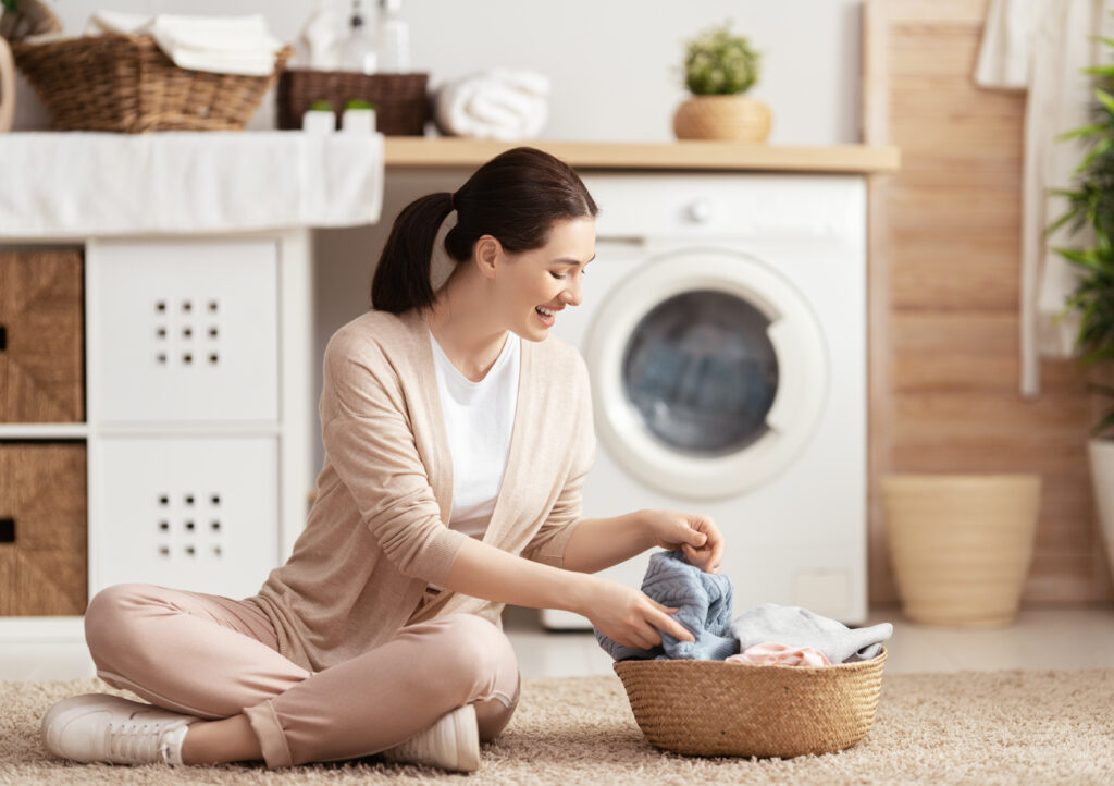 Beautiful young woman is smiling while doing laundry at home.