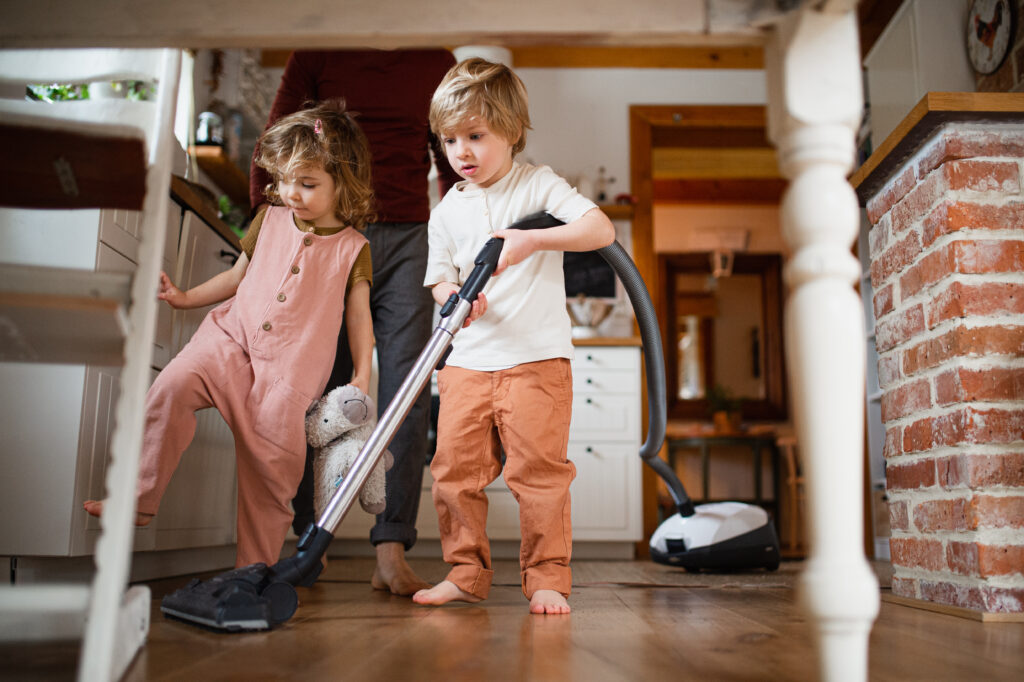 An unrecognizable father with two small children hoovering indoors at home, daily chores concept.