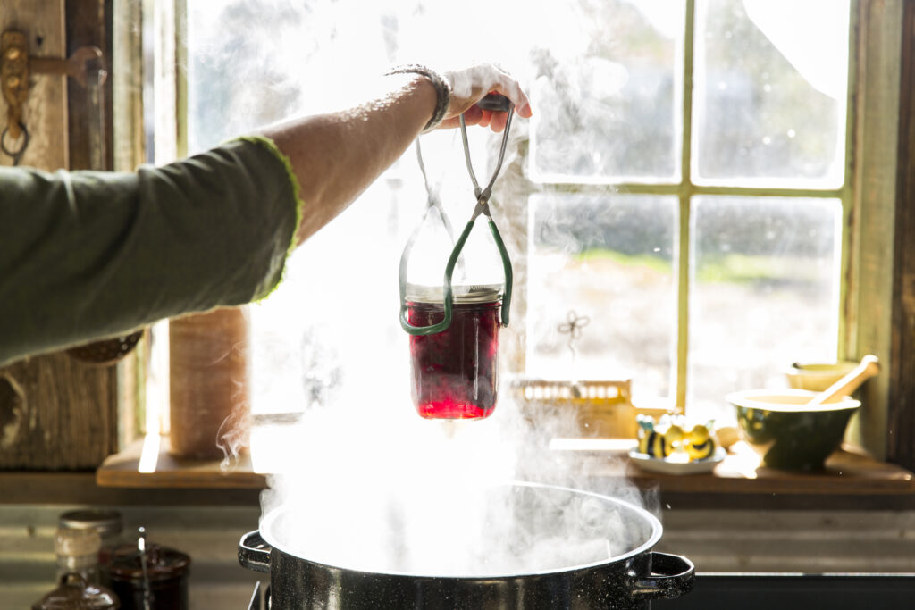 Woman's hands removing beetroot preserves jar from steaming saucepan
