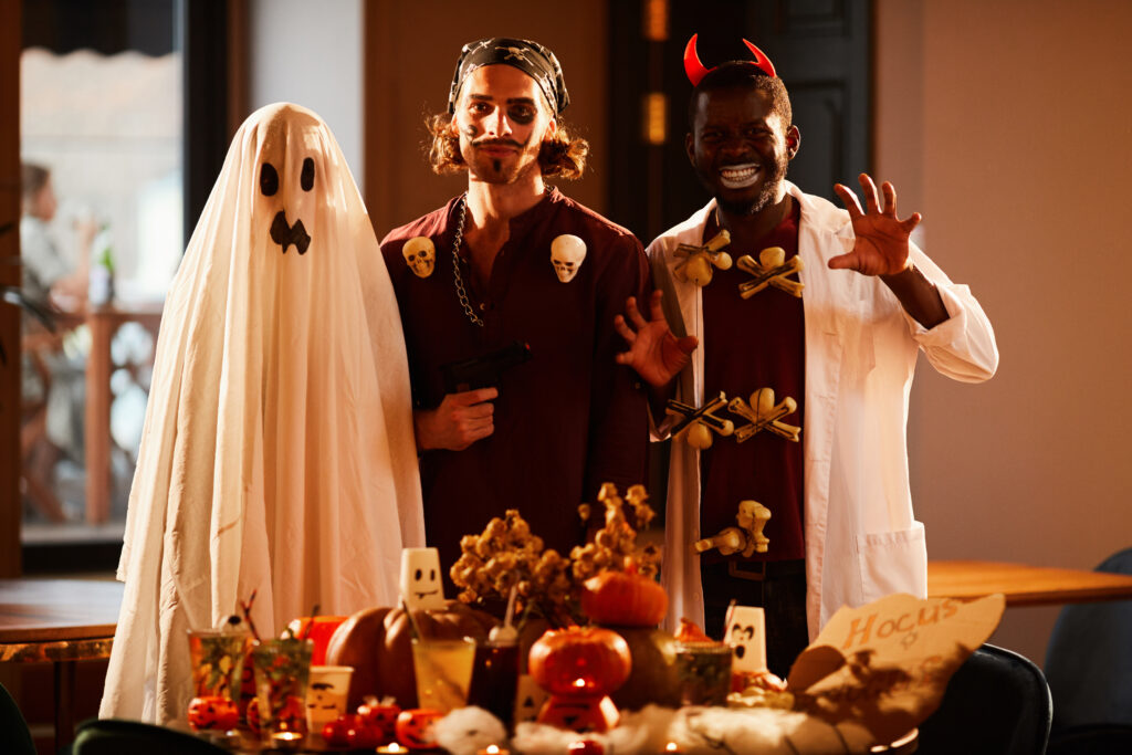 Portrait of three people wearing Halloween costumes posing by decorated table during party, copy space