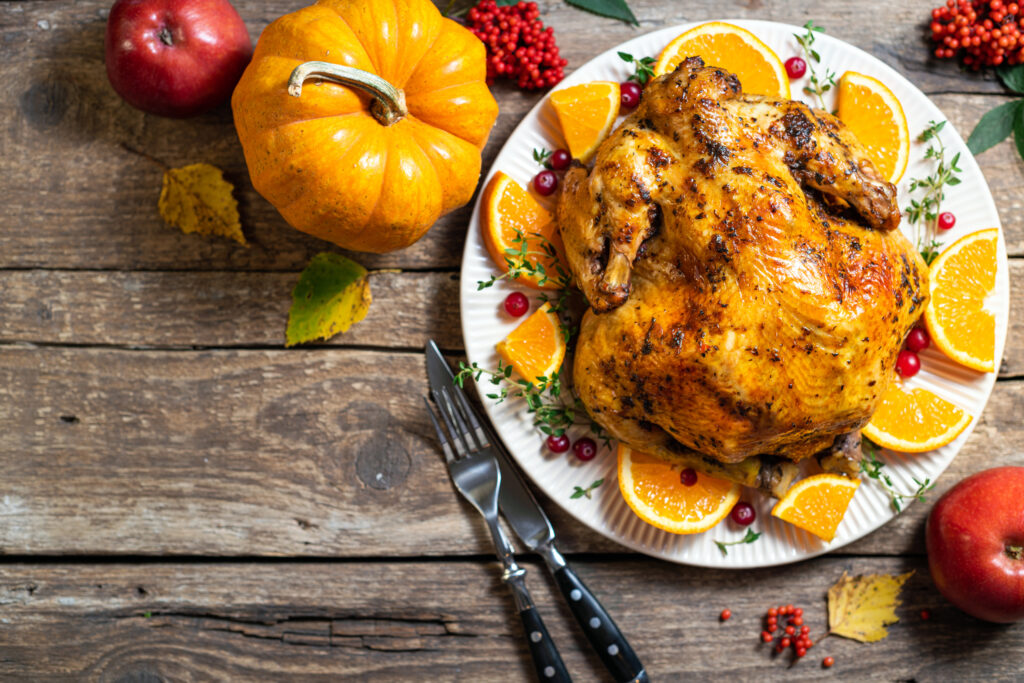 Thanksgiving background. Baked chicken or turkey with citrus and spices for celebrations for Thanksgiving Day on wooden table. Autumn table settings for Thanksgiving dinner. Top view