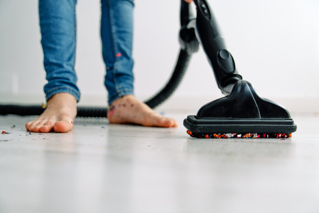 Crop anonymous barefoot male in casual jeans using vacuum cleaner for tidying floor from bright confetti